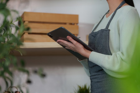 Close-up of woman holding tablet in a plant-filled workspace.
