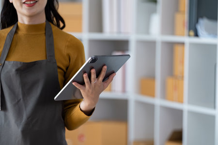 Entrepreneur in Apron Using Tablet in Modern Office Space for Small Business Management and Operationsの写真素材