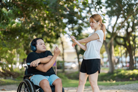 Young Woman and Man in Wheelchair Enjoying Outdoor Exercise in a Park Setting with Headphones and Fitness Gearの写真素材