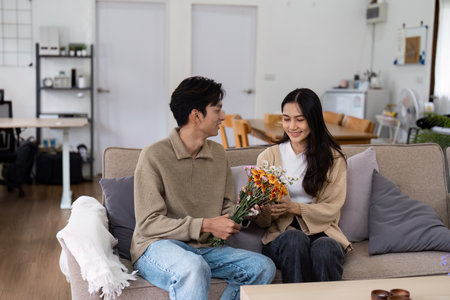 Young Couple Enjoying a Cozy Moment at Home with Flowers in a Modern Living Room Settingの写真素材