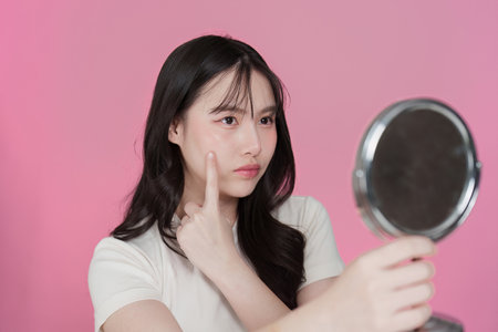 Skincare Routine. Young woman examining her skin in mirror, focusing on blemishes.の写真素材