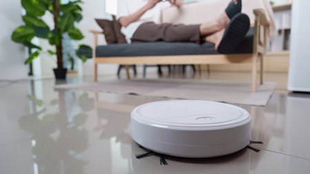 Home Automation. Robotic vacuum cleaner cleaning floor while user relaxes on couch.の写真素材