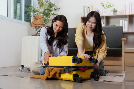 Travel Planning: Friends struggling to close their packed suitcaseの写真素材