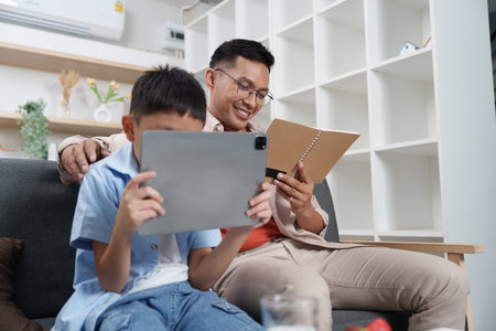 Father and son enjoying digital reading together at homeの写真素材