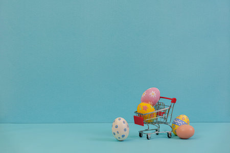 Easter shopping. Colorful eggs in a mini shopping cart on a blue background.