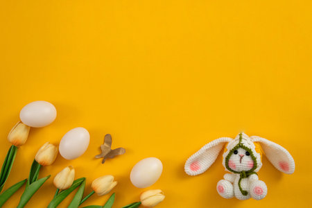 Easter Celebration. Cute bunny figurine with eggs and tulips on vibrant yellow background.