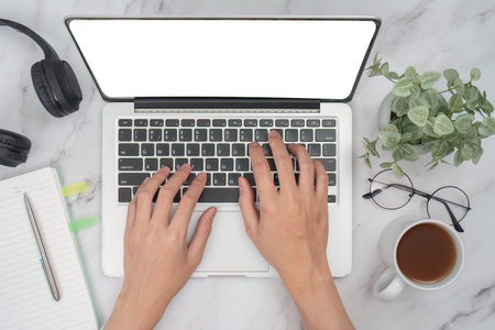 Hands typing on laptop keyboard in modern workspace with coffee