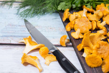 Chanterelle mushrooms lie on a dark wooden Board, bunches of dill and parsley lie on the table....