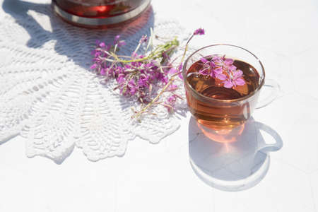 Herbal tea from fermented kipreya leaves in a glass Cup on a light background, a teapot with tea stands next to it on a lace napkin.Traditional Russian Kopor Tea (Ivan-Tea). Horizontal arrangement. Place for a copy of spaceの写真素材