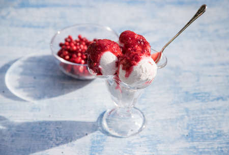 A bowl with ice cream balls and jam from red berries on a blue background, berries in a glass vase,...