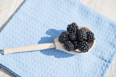 A wooden spoon with blackberries lies on a blue napkin. Close up.の写真素材