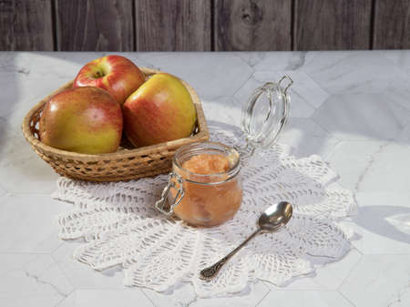 A jar of applesauce and apples in a wicker plate on a light background on a lace napkin. Horizontal...