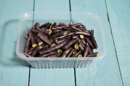 Sliced string beans in a plastic container on a colored wooden background. Source of vegetable...