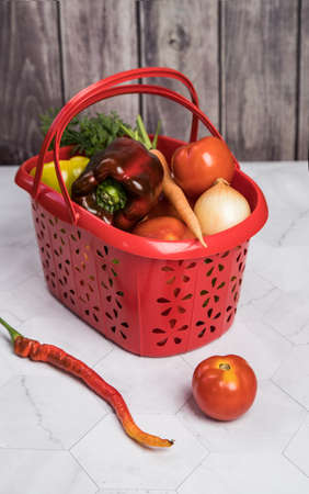 Basket with autumn harvest of vegetables-tomatoes, onions, peppers on a light background. Vertical orientationの写真素材