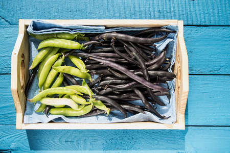 Pods of green peas and asparagus beans lie on a wooden tray on a wooden background. Source of vegetable protein. Healthy eating conceptの写真素材