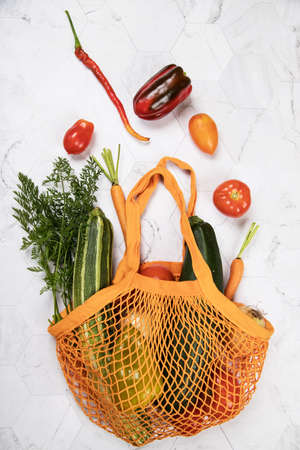 Reusable mesh shopping bag with vegetables-zucchini, tomatoes, peppers, carrots, onions, flying in...