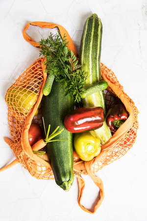 Reusable mesh shopping bag with vegetables-carrots, onions, zucchini, tomatoes, peppers, on a light...