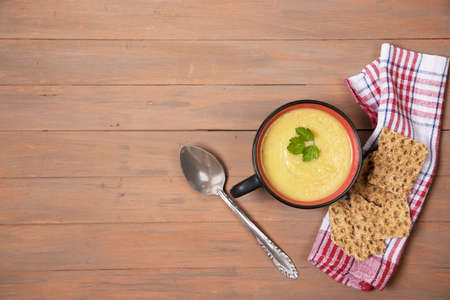 A plate of pumpkin soup, grain loaves on a red napkin and a brown wooden background. Horizontal orientation. Place for a copy spaceの写真素材