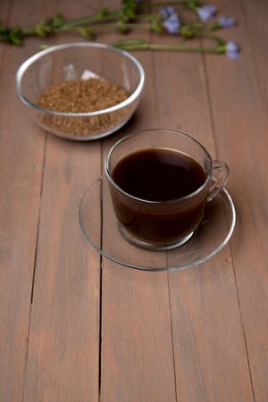 A glass Cup with a chicory drink on a dark brown wooden background, a plate with chicory, a chicory flower. A place for a space mine .Vertical orientationの写真素材