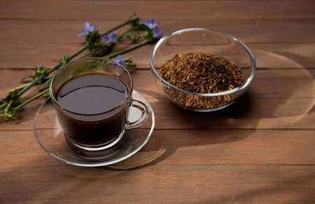 A sunbeam illuminates a chicory drink in a glass Cup on a brown wooden background, with a chicory flower in the background. Horizontal orientationの写真素材