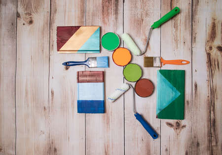 The concept of self-repair of an apartment or house. Paints and brushes are laid out on a wooden surface along with test paint strokes. Place for a copy spaceの写真素材