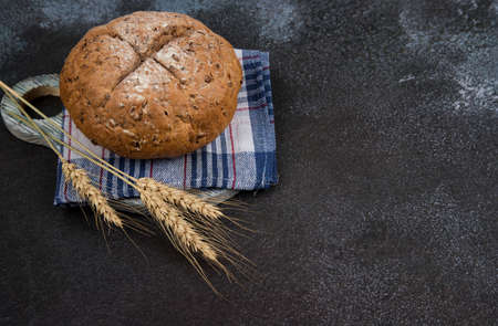 Homemade bread on a checkered napkin with spikelets, dark cutting Board, dark background. Place for...