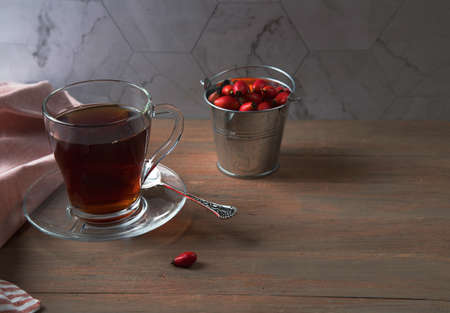 A Cup of vitamin tea with rosehip and a tin bucket of fruit on a brown wooden background. Natural...