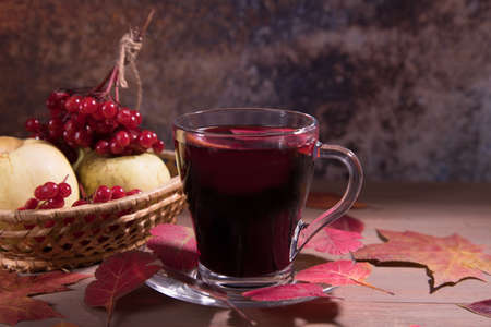 Drink mulled wine in a glass Cup on a dark wooden background with autumn leaves, viburnum berries...