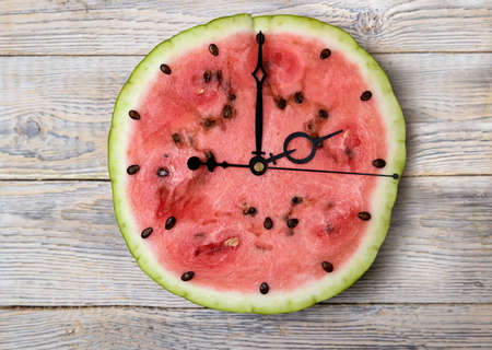 Watermelon slice with arrows showing ten o'clock, light wooden background. Horizontal orientation
