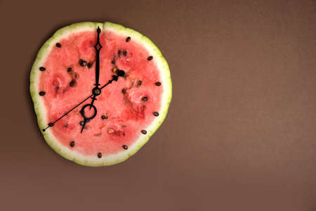 Cut of a ripe watermelon in the form of a clock, the hands show seven, brown background. Horizontal...