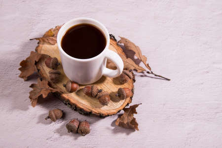 White acorn coffee Cup on a wooden section with acorns and oak leaves on a light background....