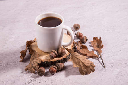 Coffee Cup made of acorns on a wooden cut with acorns and oak leaves, light background. Coffee substitute, close-up.Horizontal orientation.の写真素材