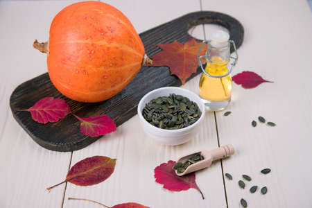 Healthy pumpkin oil with pumpkin seeds and autumn leaves on a light background.の写真素材