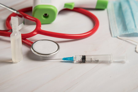 The doctor's equipment consists of a syringe with a virus vaccine, an infrared thermometer, a stethoscope and a medical mask.の写真素材