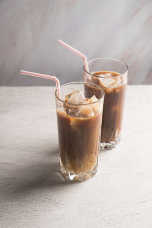 Cold coffee with milk and ice in tall glasses with tubes on a light background.