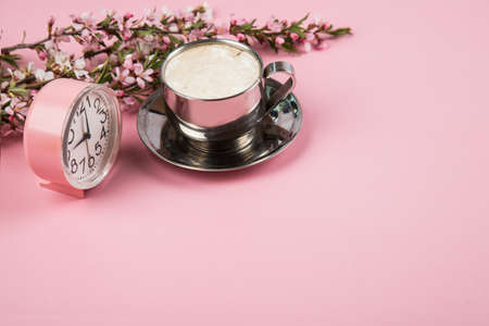 A cup of morning cappuccino with a pink alarm clock on a pink paper background.の写真素材