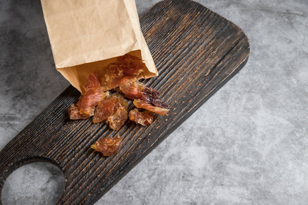 Pieces of dried meat are poured out of the craft bag onto a wooden cutting board.の写真素材