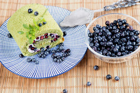 Homemade cakes in the form of a sponge roll with berries and matcha tea on a woven straw background.