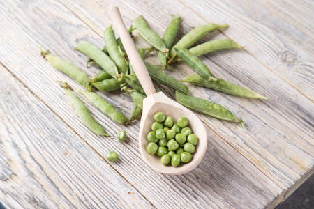 Top view of a wooden spoon with green peas on a light wooden table.の写真素材