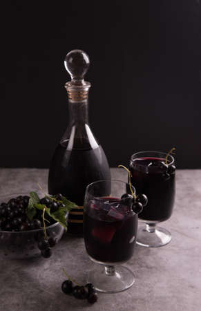 Homemade black currant liqueur in a glass and decanter on a dark background.の写真素材