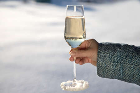 A womans hand in a warm jacket holds a glass of snow-covered champagne.の写真素材