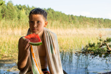 Family vacation in nature, a child eats a juicy watermelon on the shore of the lake.の写真素材