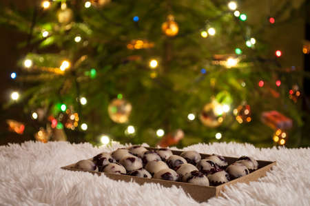 Closeup of handmade sweets of marzipan and cranberries for Christmas with background of Christmas tree with colorful lightsの写真素材