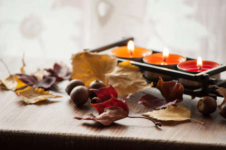Dry colorful autumn leaves and acorns of northern red oak on wooden board with three burning candles in backgroundの写真素材