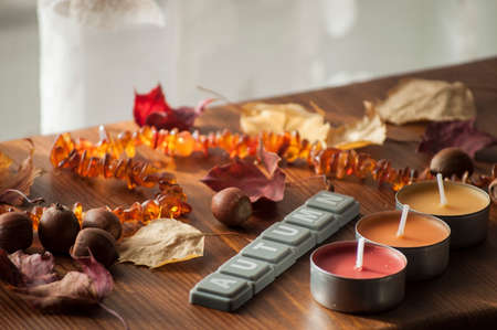Background for autumn mood with candles, colorful dry autumn leaves and acorns of northern red oak and amber necklace in sunlightの写真素材