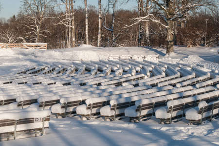 Seats covered with thick layer of snow in open-air stage on sunny day of winterの写真素材