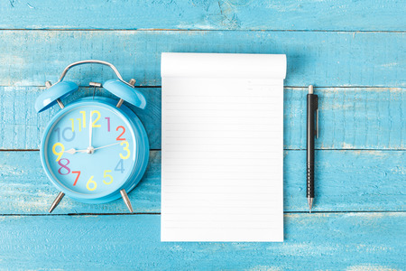 White lined note paper with blue clock on blue wood table for background