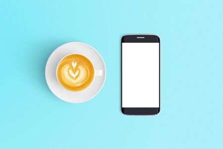 Top view of Cup of coffee in a white cup and smart phone on office desk backgroundの写真素材