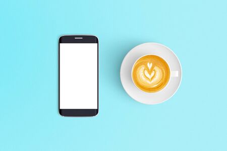 Top view of Cup of coffee in a white cup and smart phone on office desk backgroundの写真素材