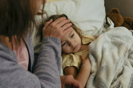 Portrait of sad engrossed sick little girl and her mother touching daughters foreheadの写真素材